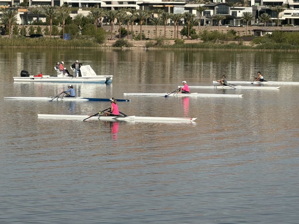 Rowers on the lake with waterfront homes and palm trees in the background